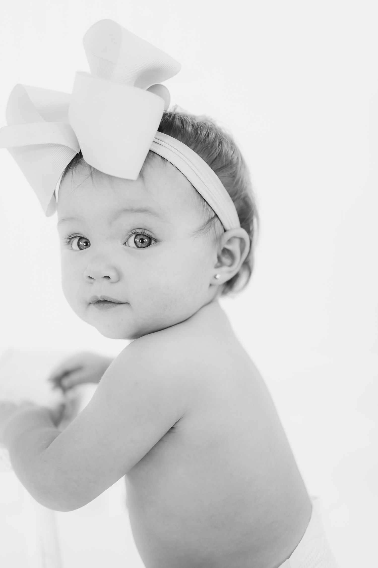High key black and white portraits of an infant wearing a white bow headband.