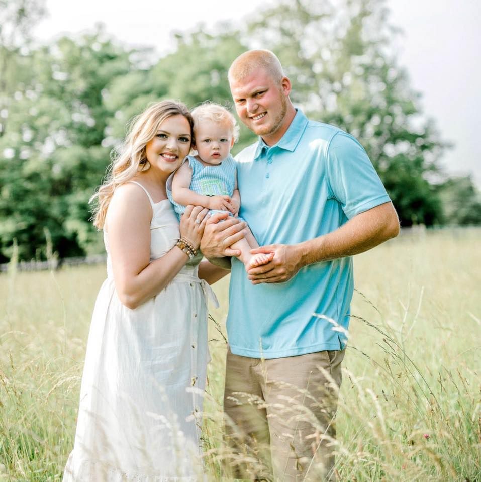 A sunny outdoor family portrait taken in a serene grassy field during golden hour.