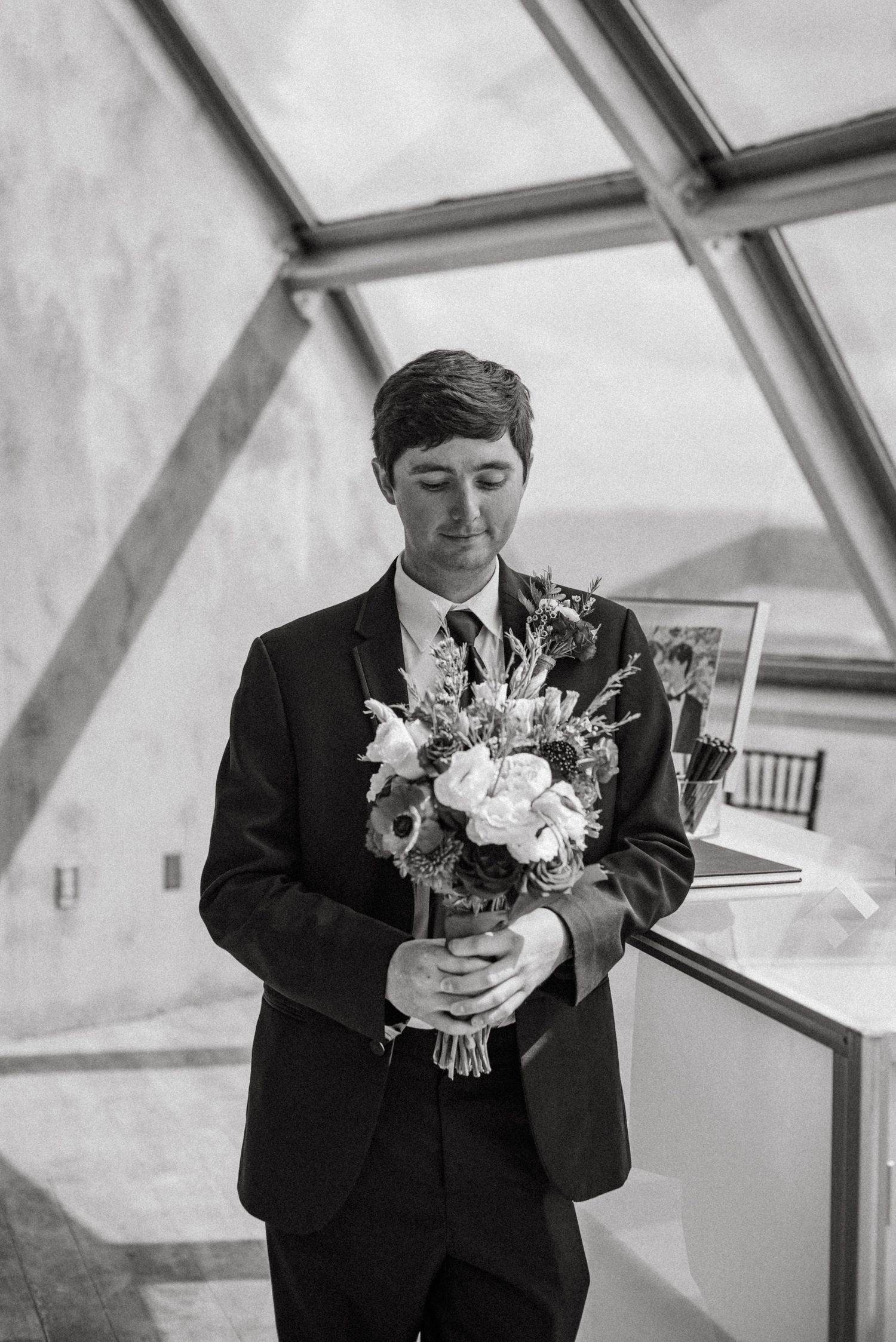 Black and white series showing person in suit holding white floral bouquet.