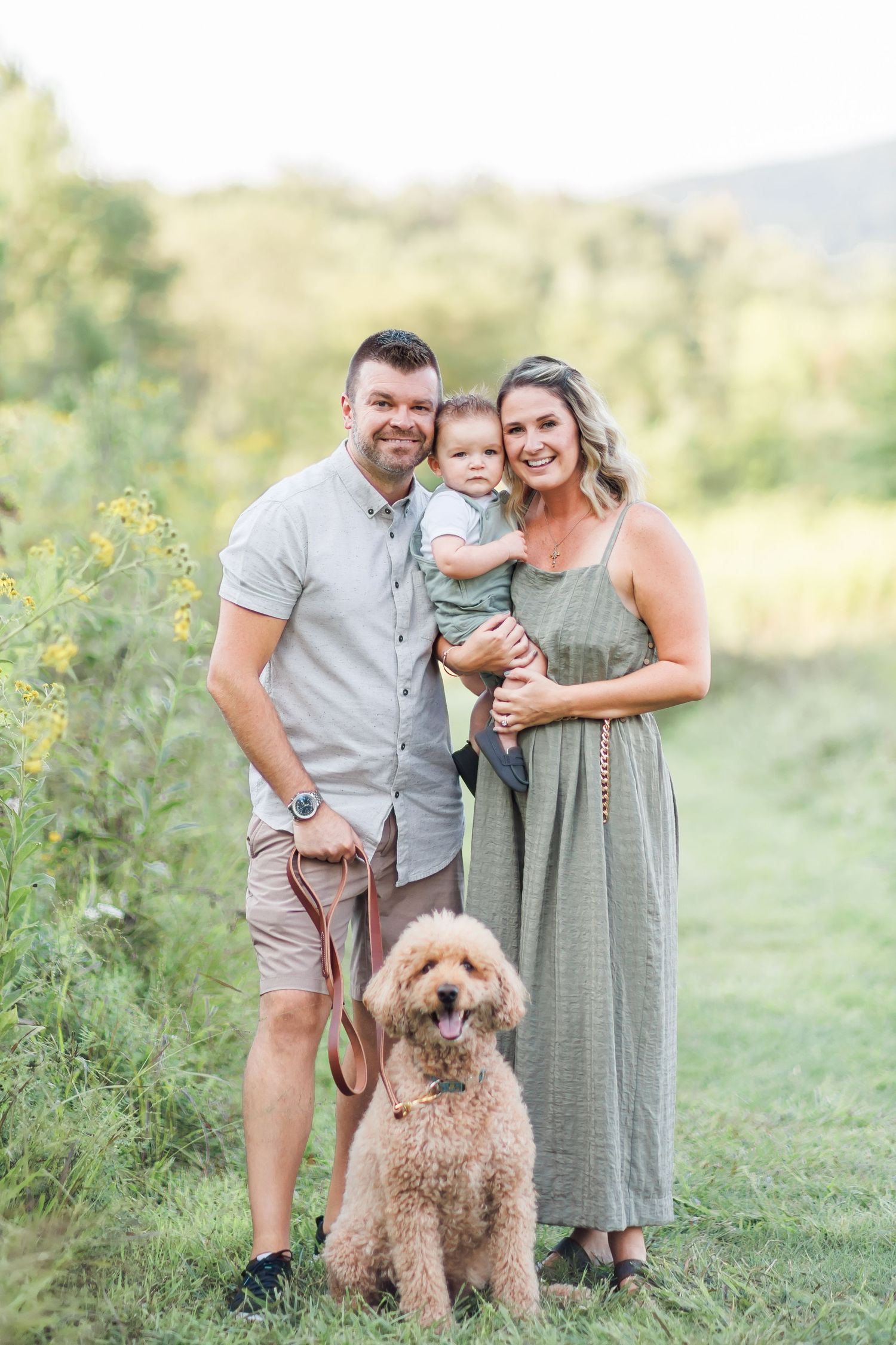 Family portrait with goldendoodle dog in a scenic summer meadow setting.