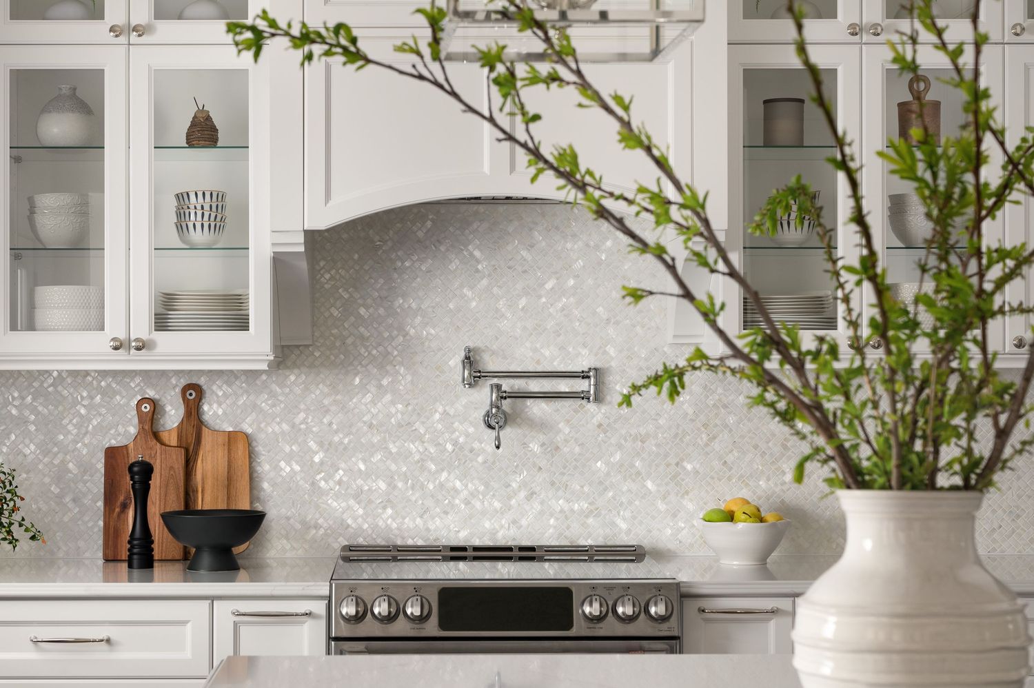 Elegant white kitchen featuring spring branches in vase and wooden cutting boards.