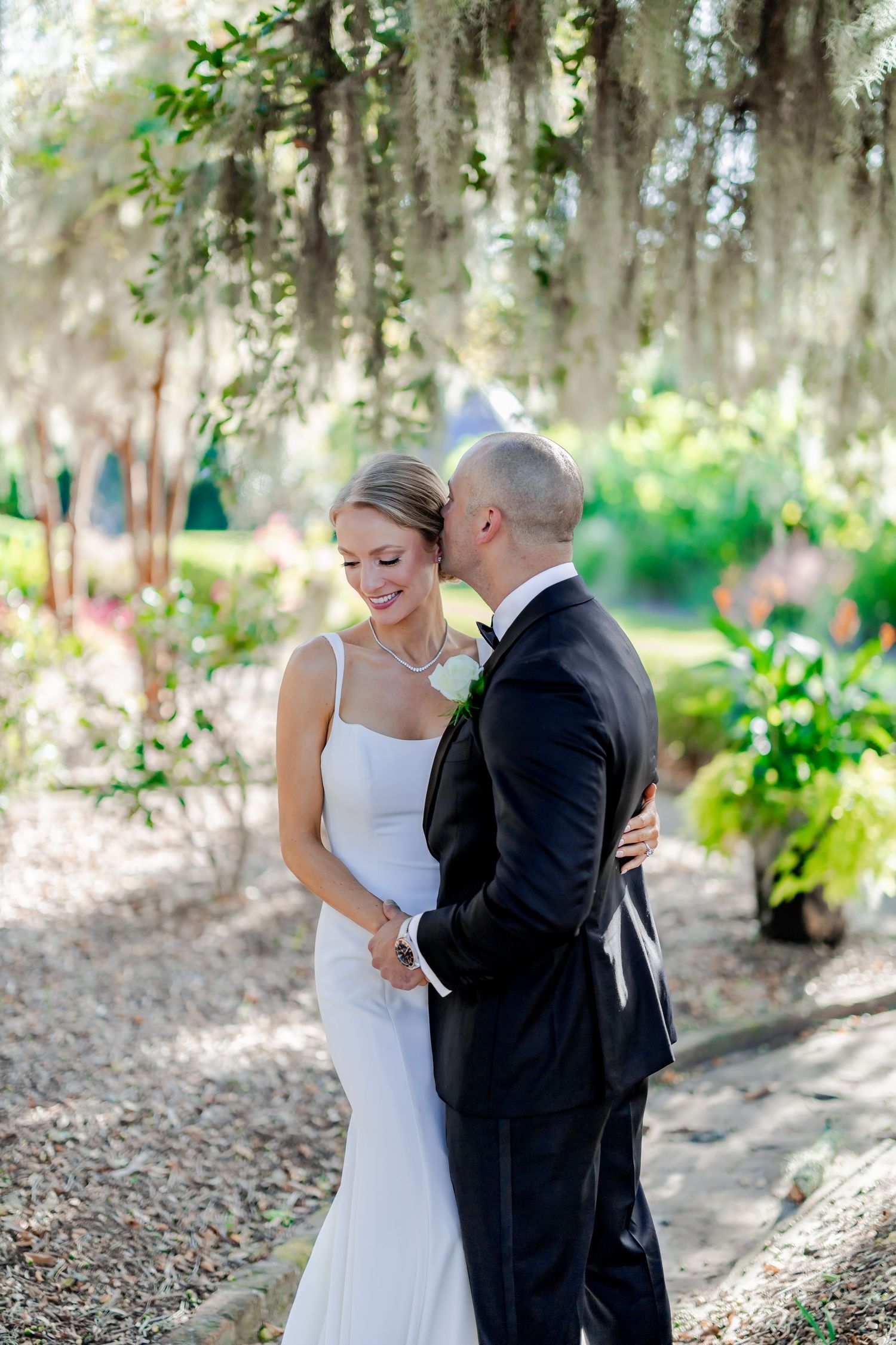 An intimate wedding moment captured under Spanish moss in a garden setting.
