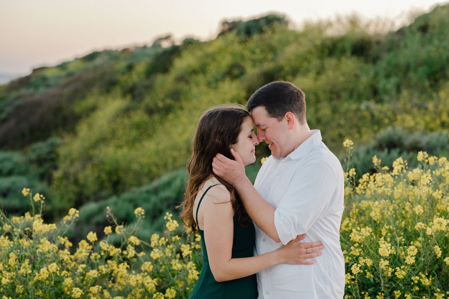 A tender moment shared between two people among blooming yellow wildflowers on a coastal hillside.