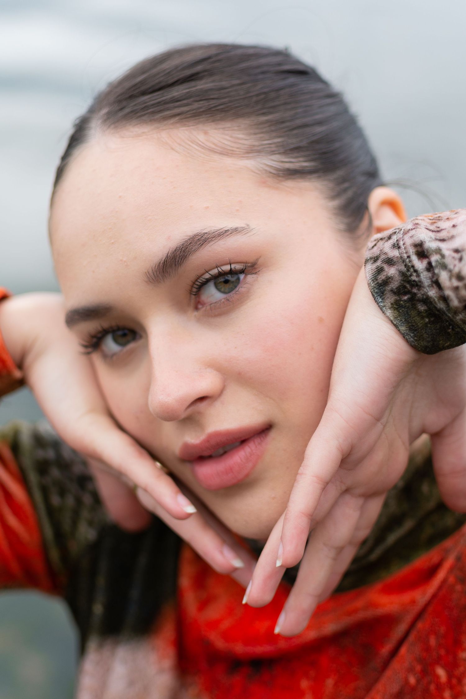 Close-up beauty portrait of someone in a red outfit framing their face with hands.