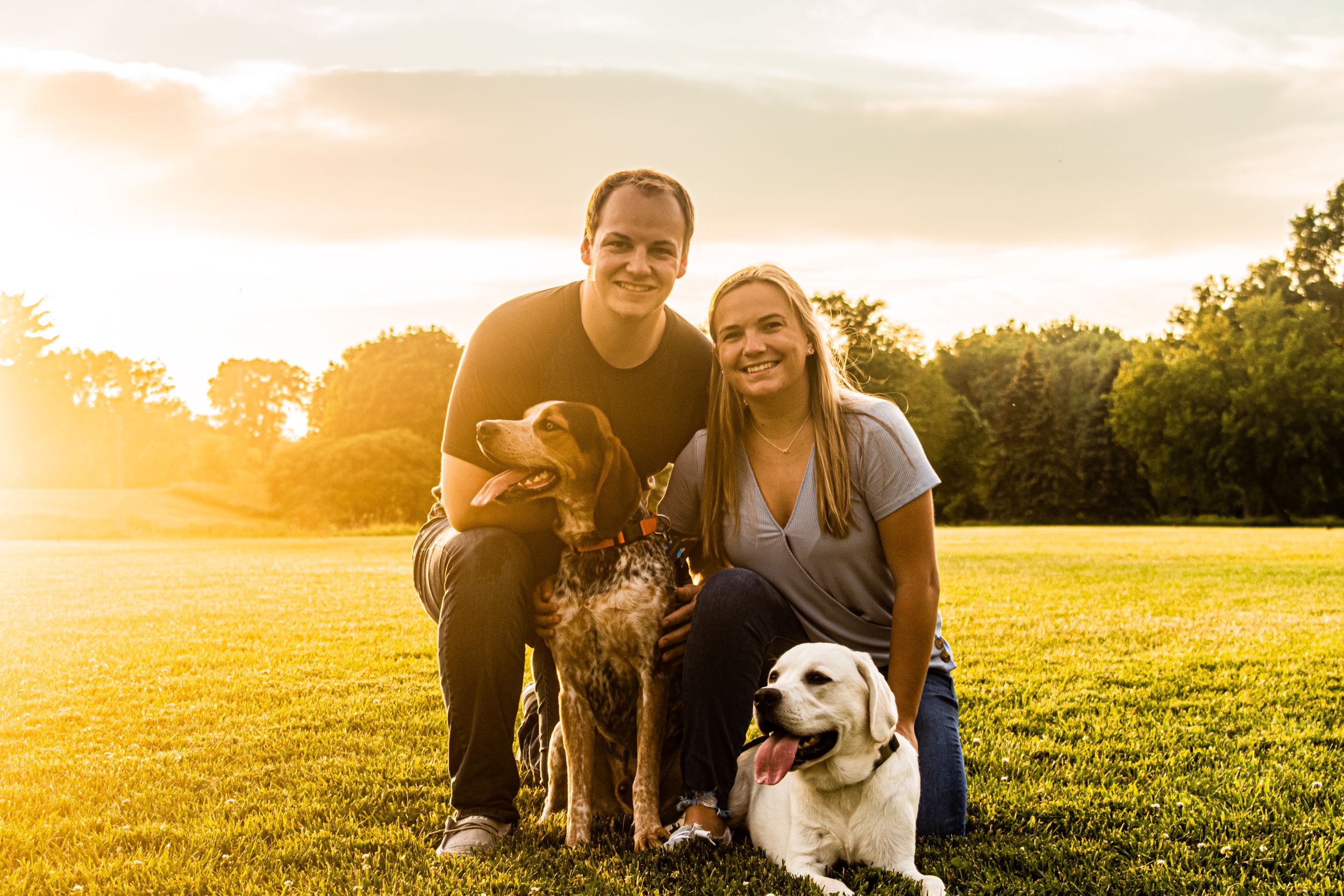 Family and their two dogs posing together in a sunny field at sunset.
