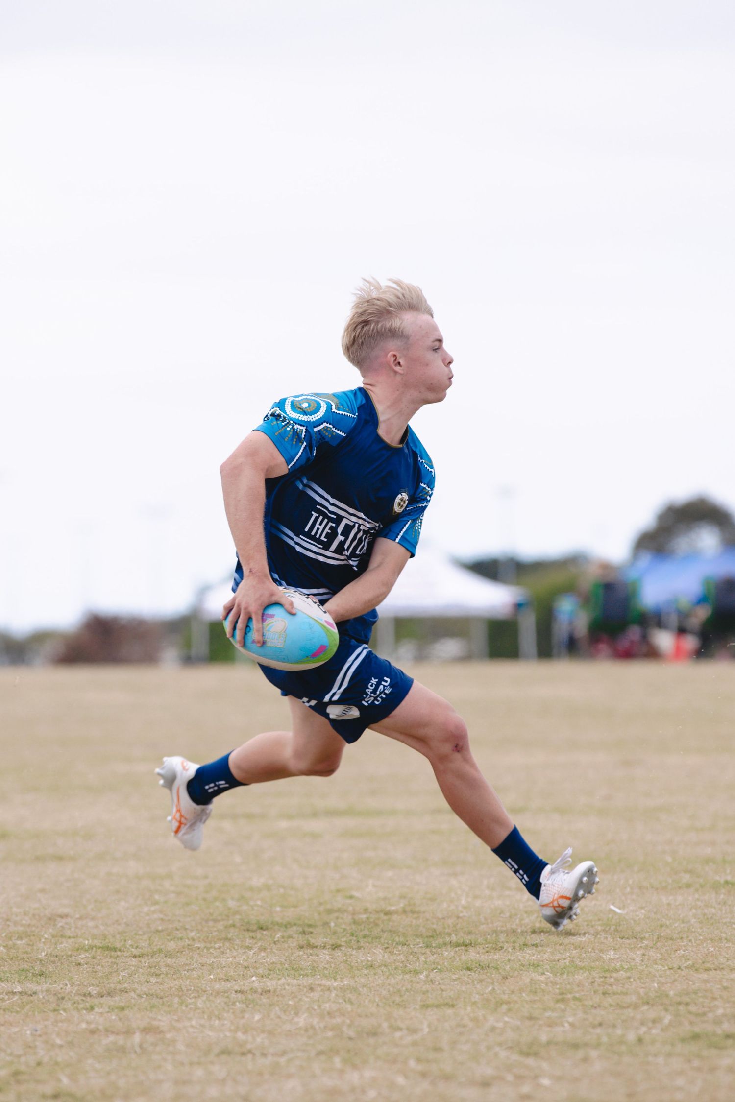 Rugby player in navy blue uniform sprinting across field with ball in hand.