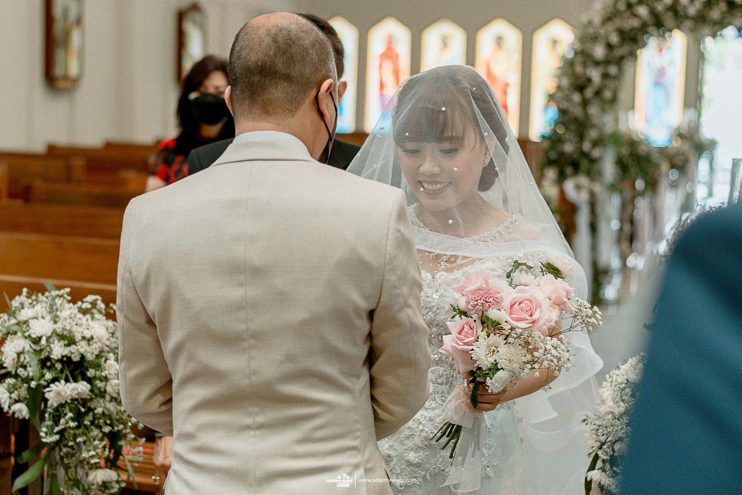 Intimate church wedding ceremony with bride holding pink bouquet and wearing lace veil.