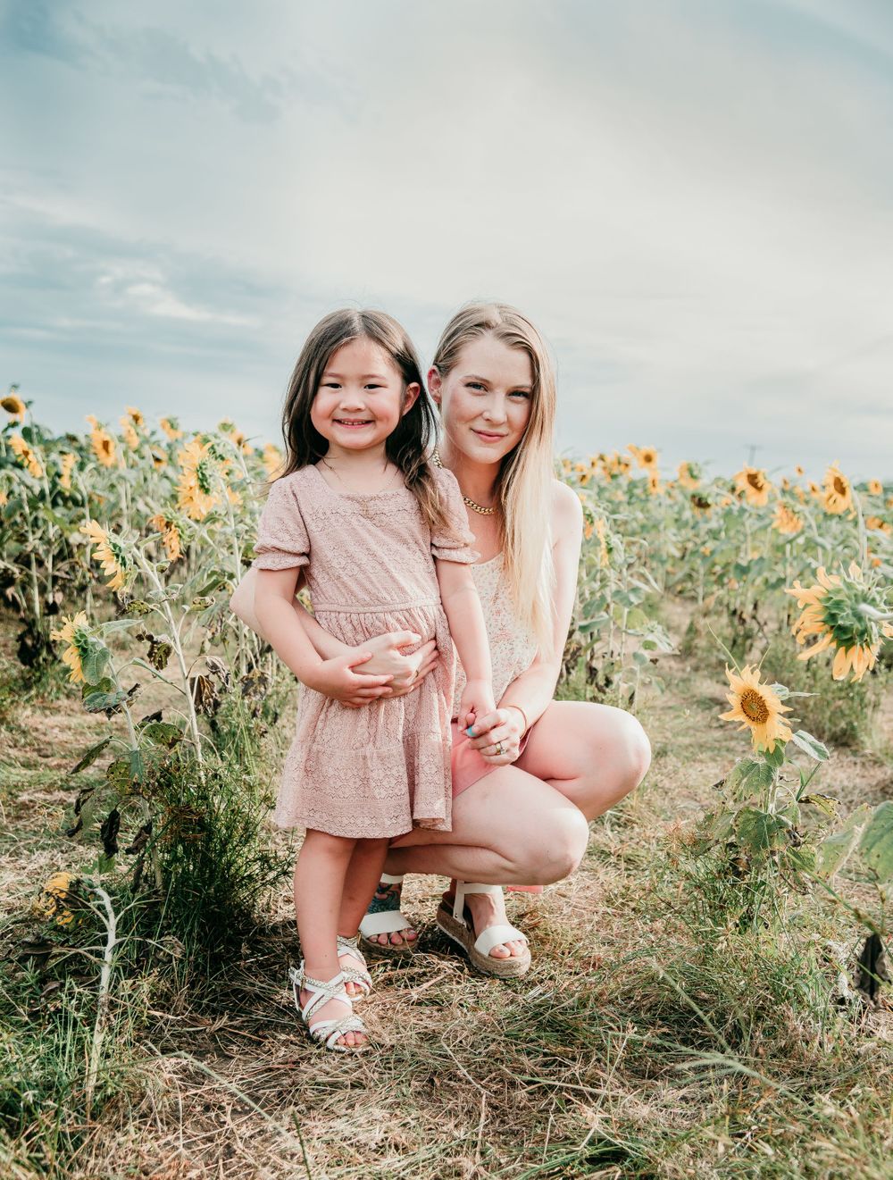 Sweet portrait in a blooming sunflower field with matching pink outfits.