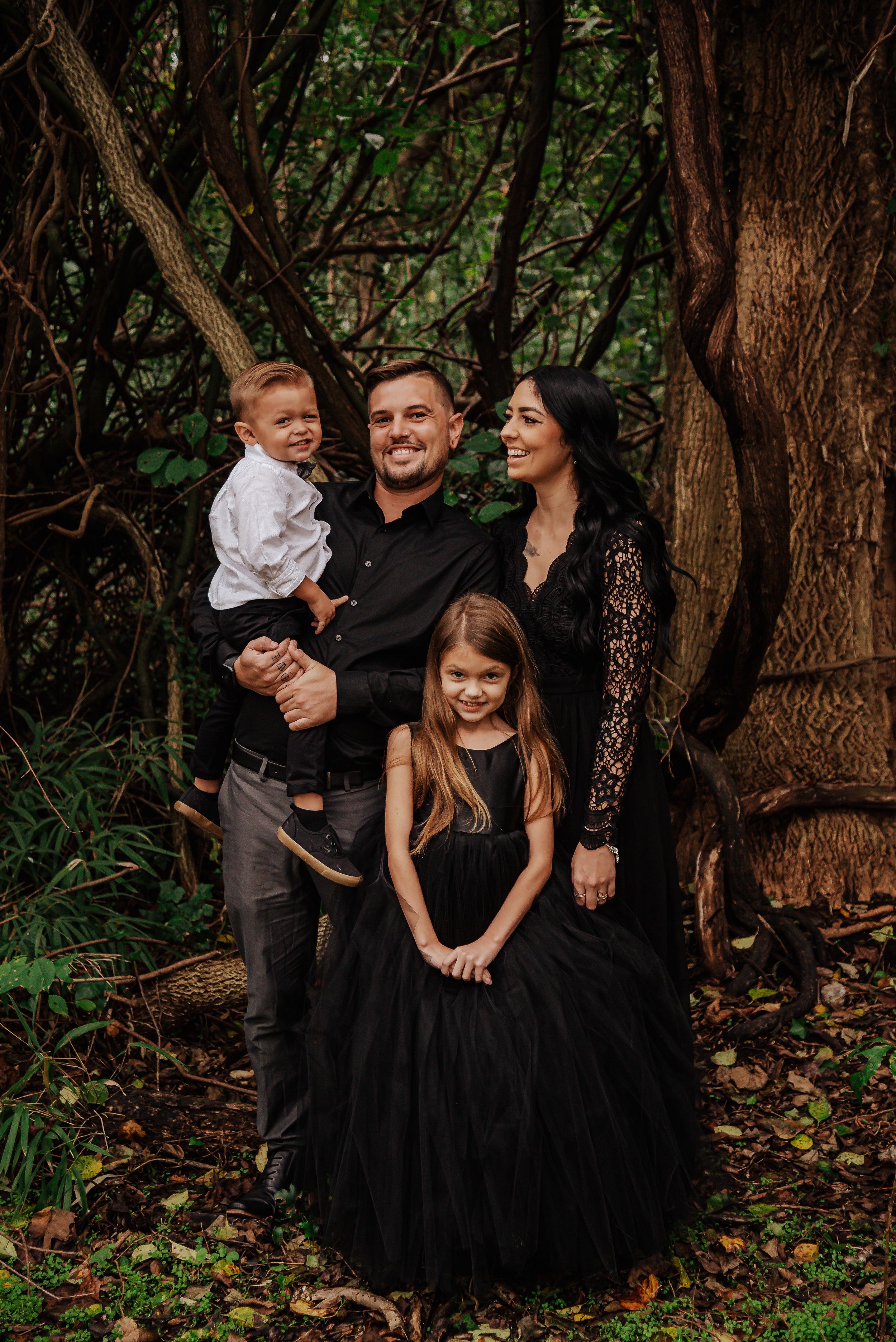 Stylish family portrait in wooded setting wearing coordinated black formal attire.