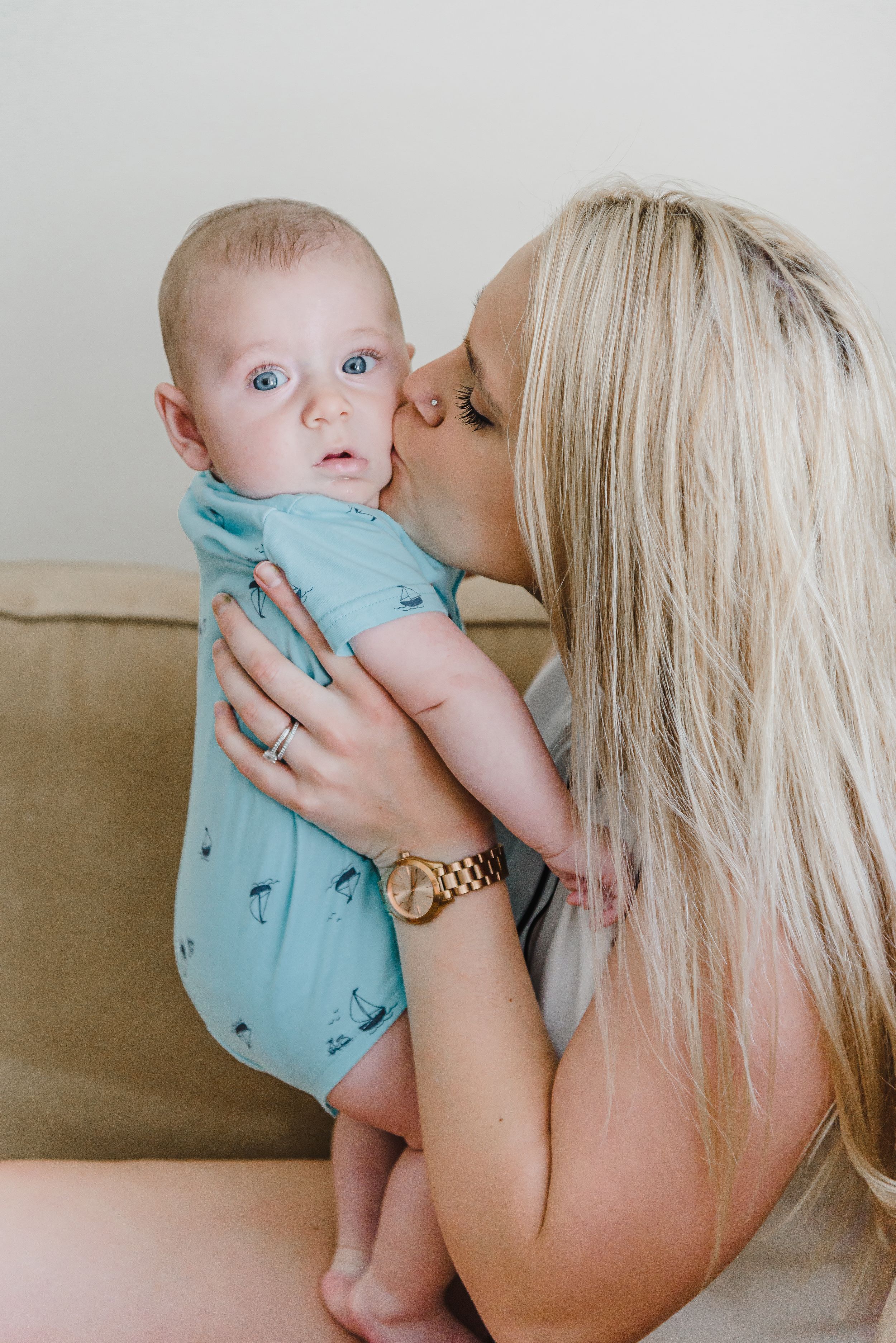 Tender moment between parent and baby in light blue onesie on beige couch.