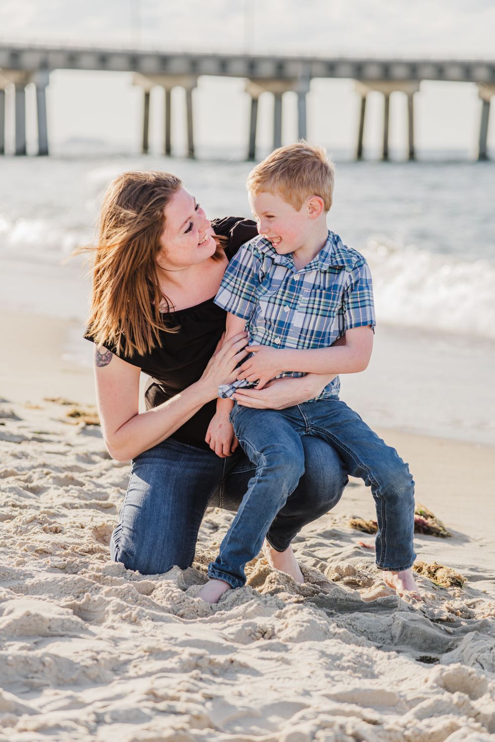 A heartwarming beach scene with two people sharing a joyful moment in front of a pier.