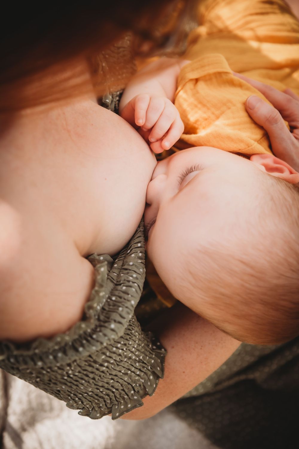 Close-up intimate nursing moment with baby in yellow outfit and gray knit wear.