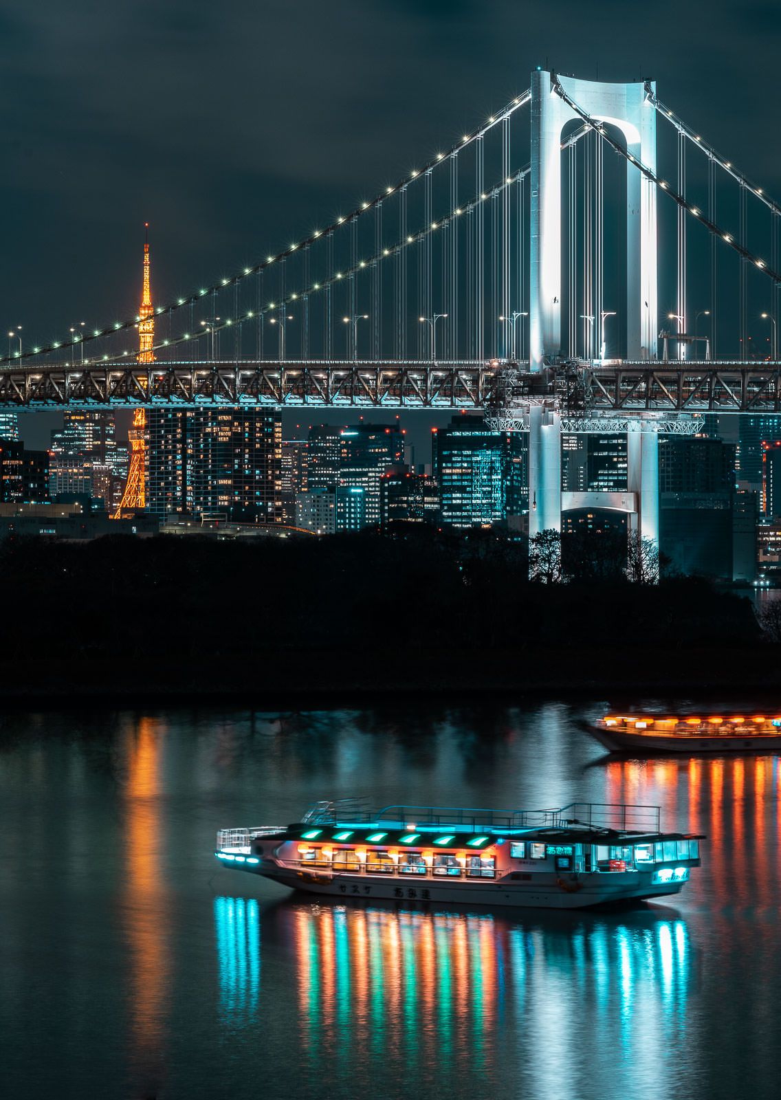 Rainbow Bridge illuminated over Tokyo Bay at night with a lit-up cruise ship passing underneath.