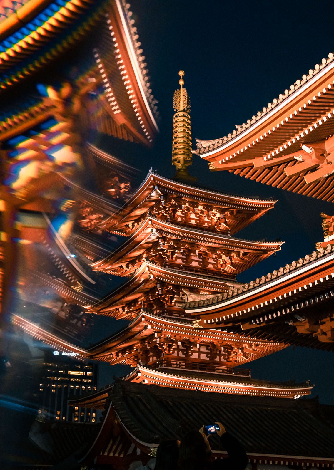 Traditional Japanese pagoda temple illuminated in warm golden light against dark blue night sky.