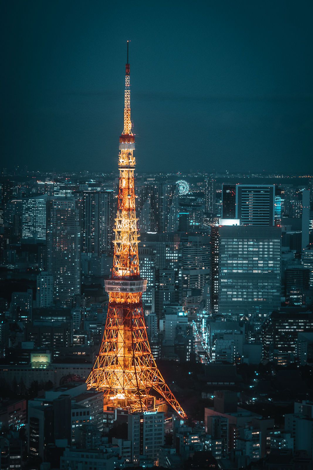 Tokyo Tower glowing orange against the dark cityscape at night with surrounding illuminated buildings.