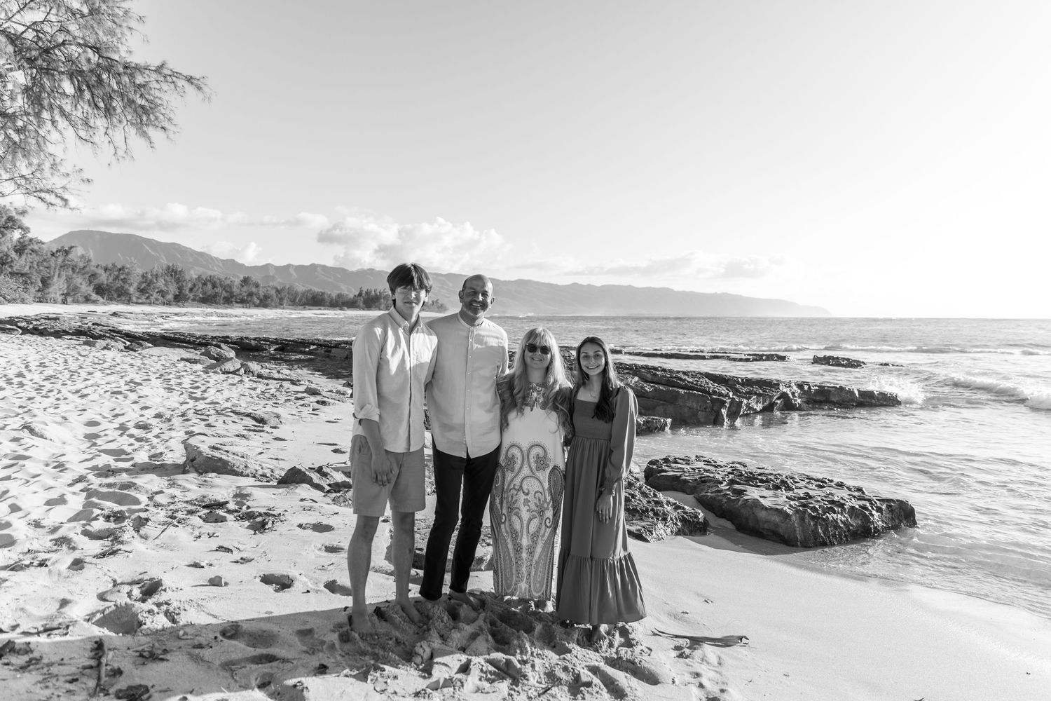 A group stands together on a scenic Hawaiian beach with volcanic rocks and mountains in the background.