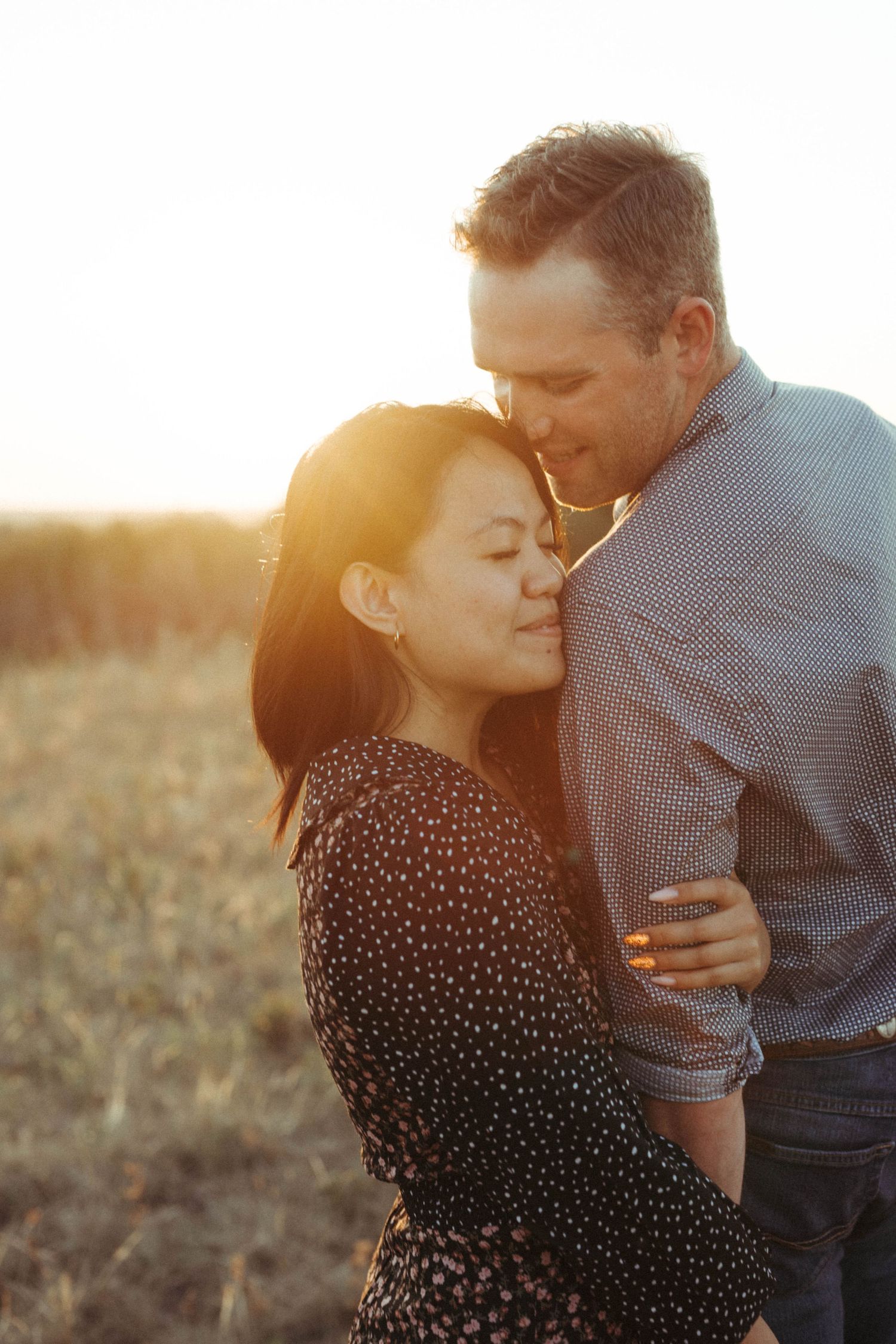 Intimate sunset portrait of couple embracing in field with golden backlighting.