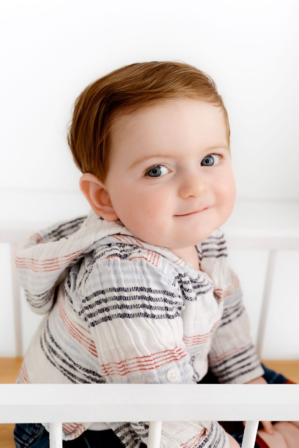 Close-up portrait of a baby wearing a striped shirt with soft lighting against white background.