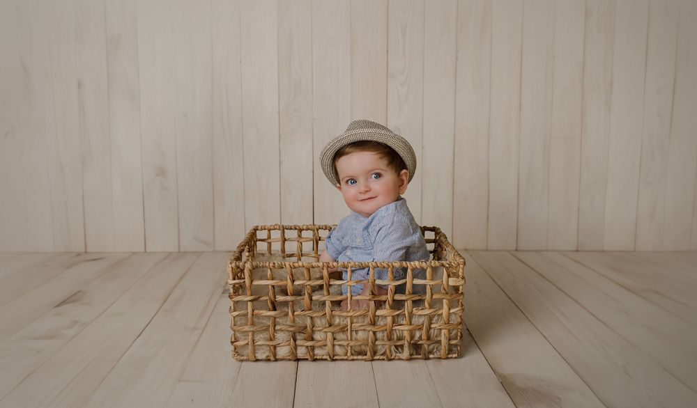 Baby sits among decorative wooden crates against white paneled wall.