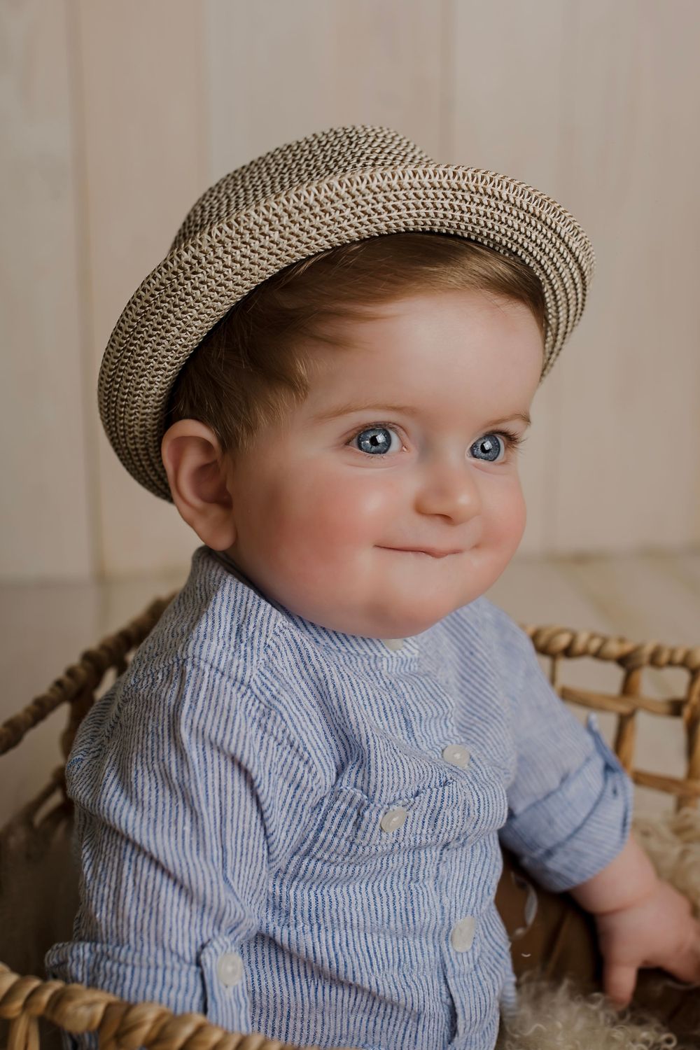 Baby in striped shirt and newsboy cap poses against neutral backdrop.
