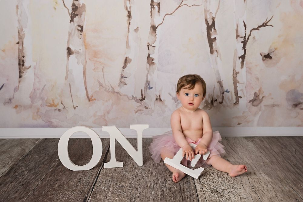 White letters spelling ONE arranged on a rustic wooden floor with vintage backdrop.
