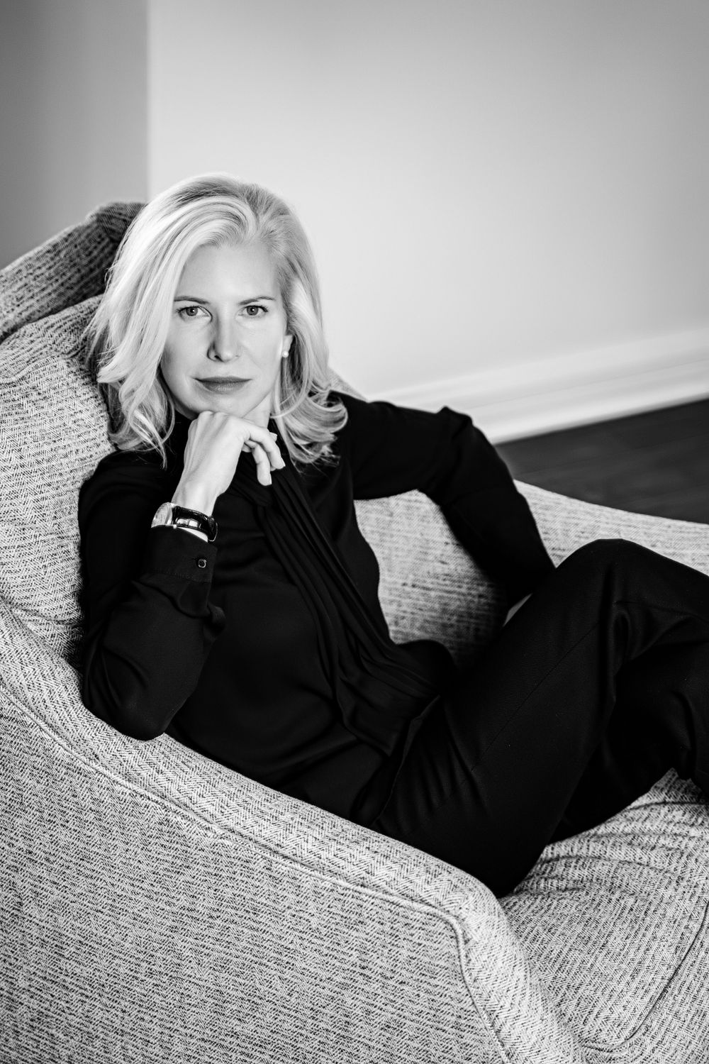 Artistic black and white portrait of woman in dark outfit lounging on grey sofa.