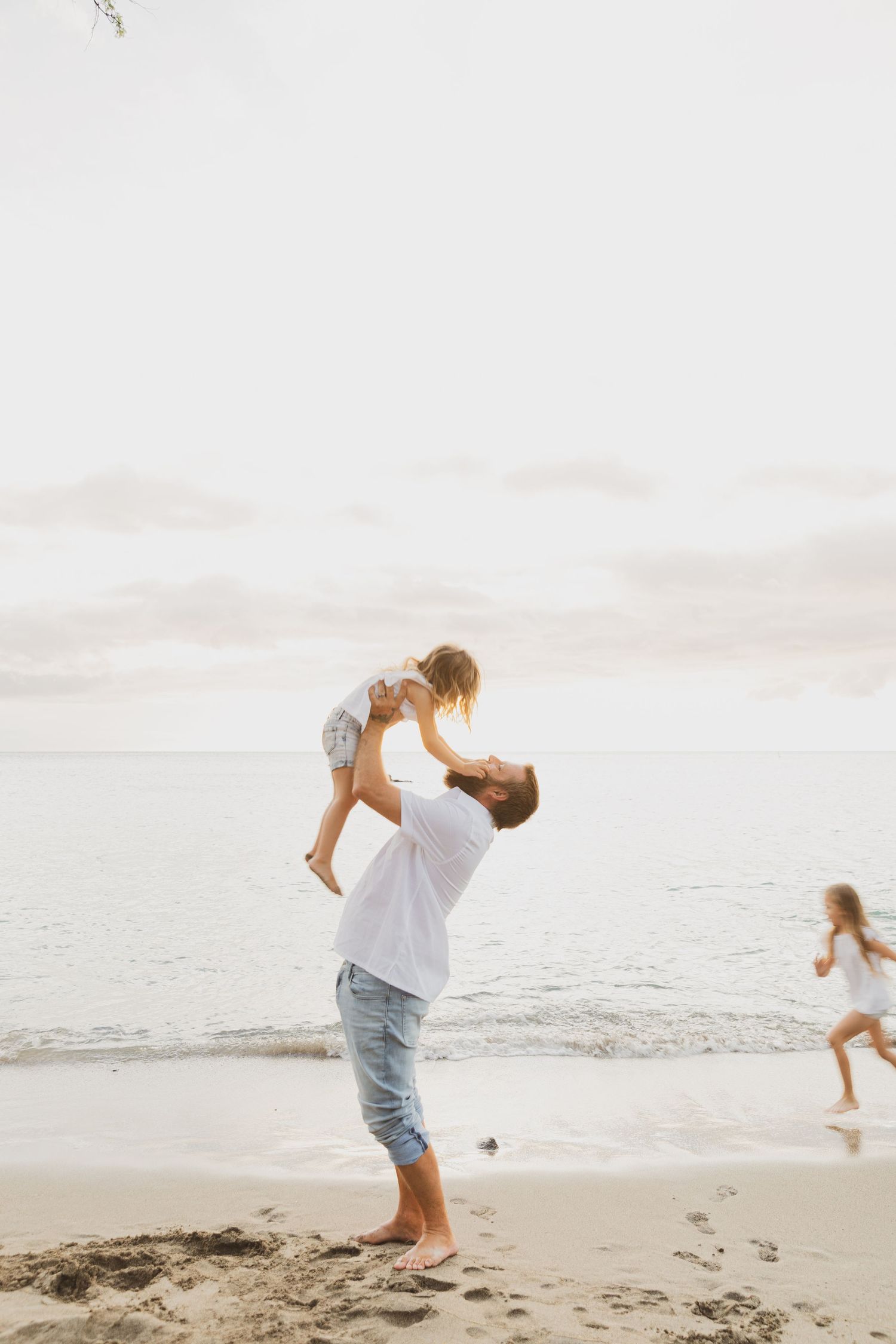 Parent lifting child playfully at the beach during sunset.