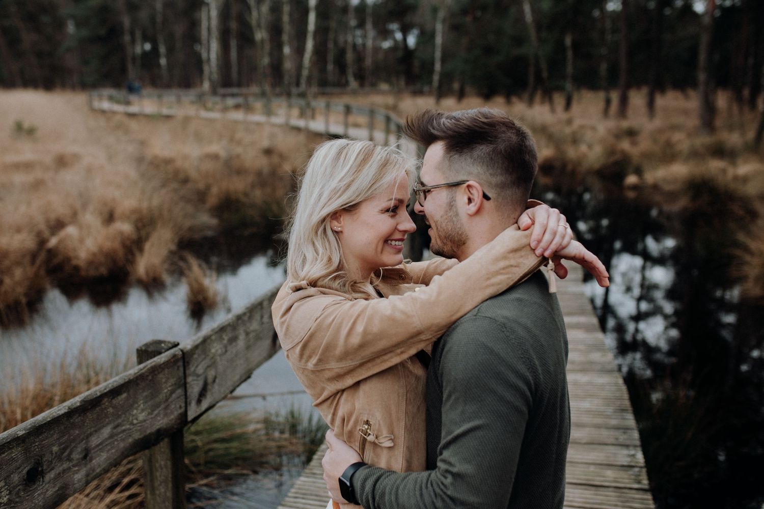 Couple embracing and smiling on a wooden dock surrounded by autumn wetlands.