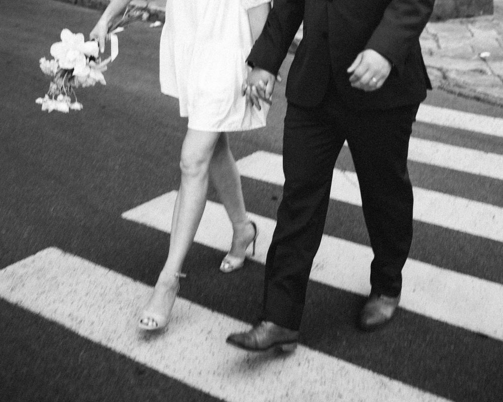 Black and white photo of feet walking across a zebra crossing with a bouquet.
