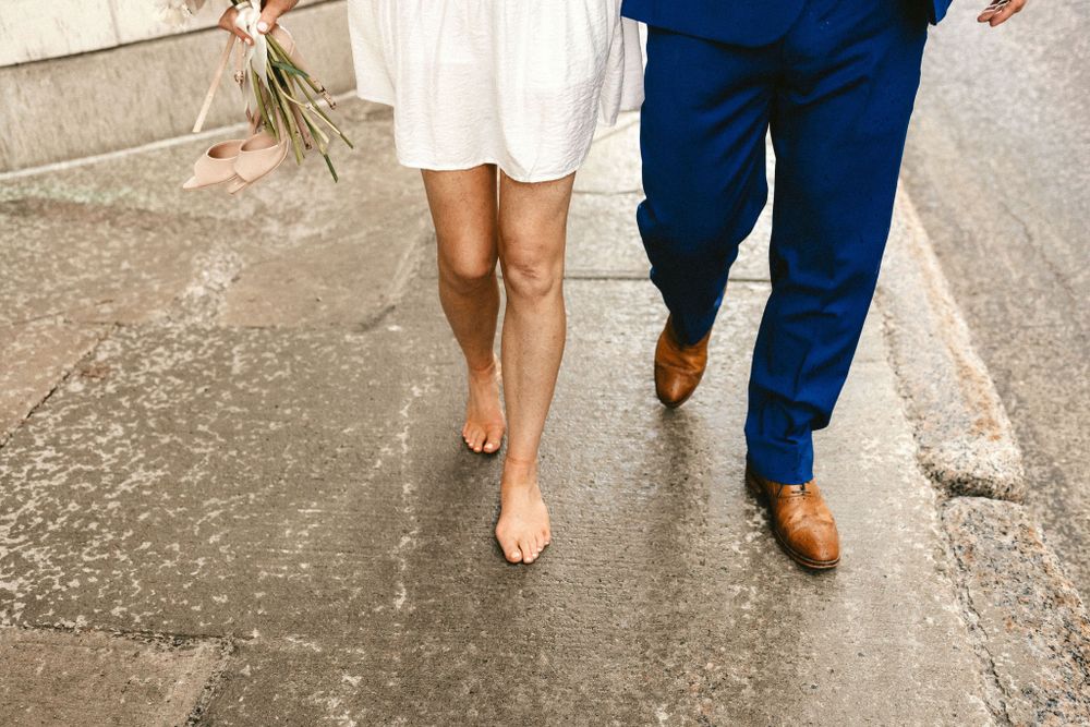 Close-up of walking feet, showing a white dress hem and blue suit pants with brown shoes.