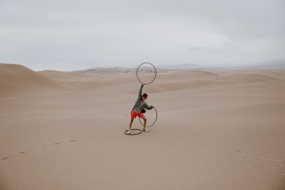 Figure with hoop performs artistic movements against desert landscape.