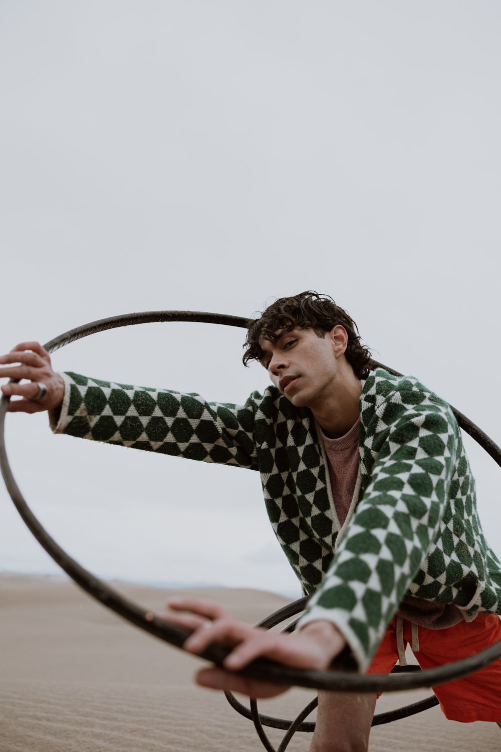 Person in polka dot jacket poses creatively with large hoop in desert setting.