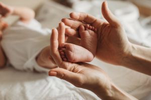 Parent hands tenderly holding and massaging newborn baby tiny feet on white blanket.