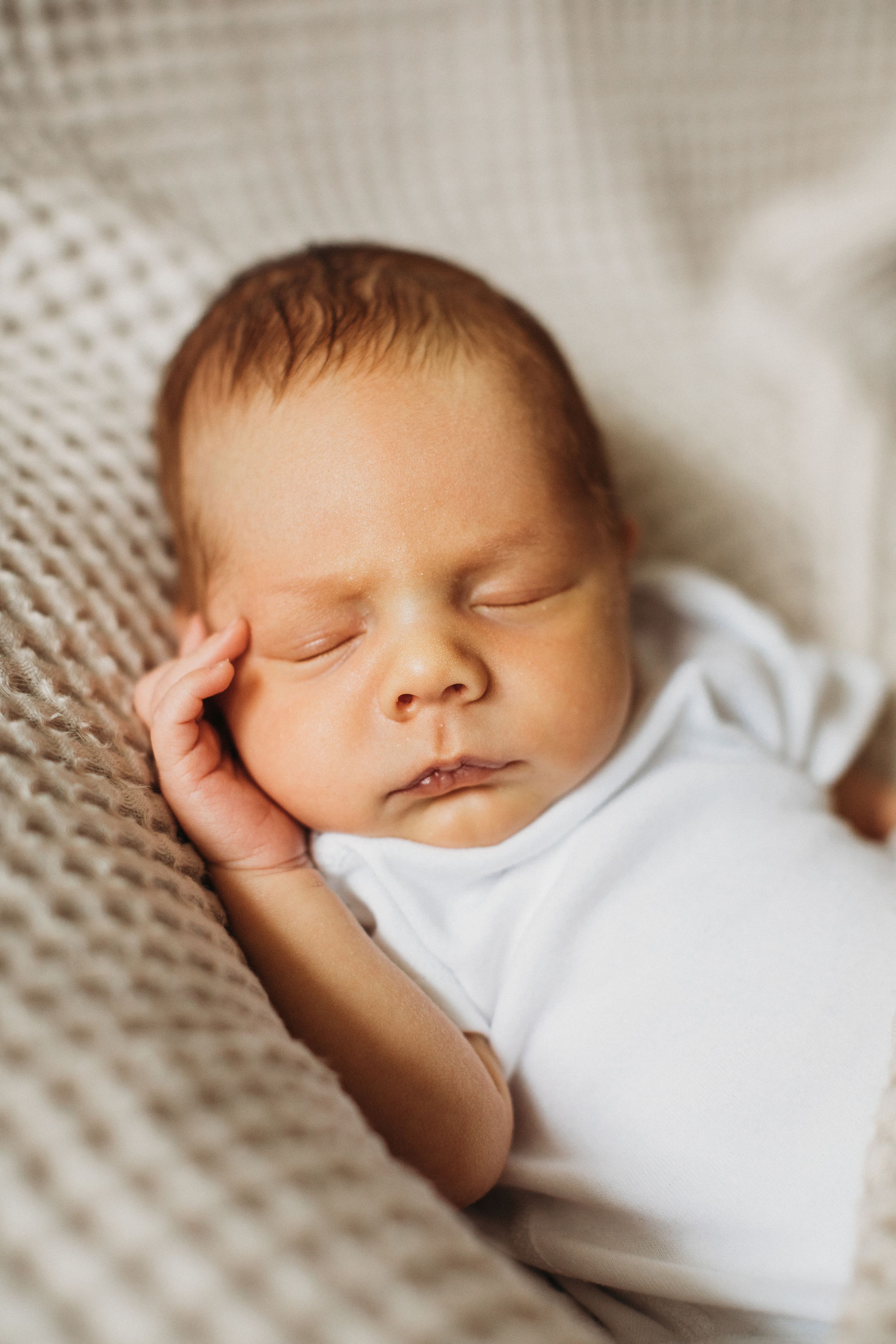 Peaceful newborn baby sleeping on a soft knit blanket in a white onesie.