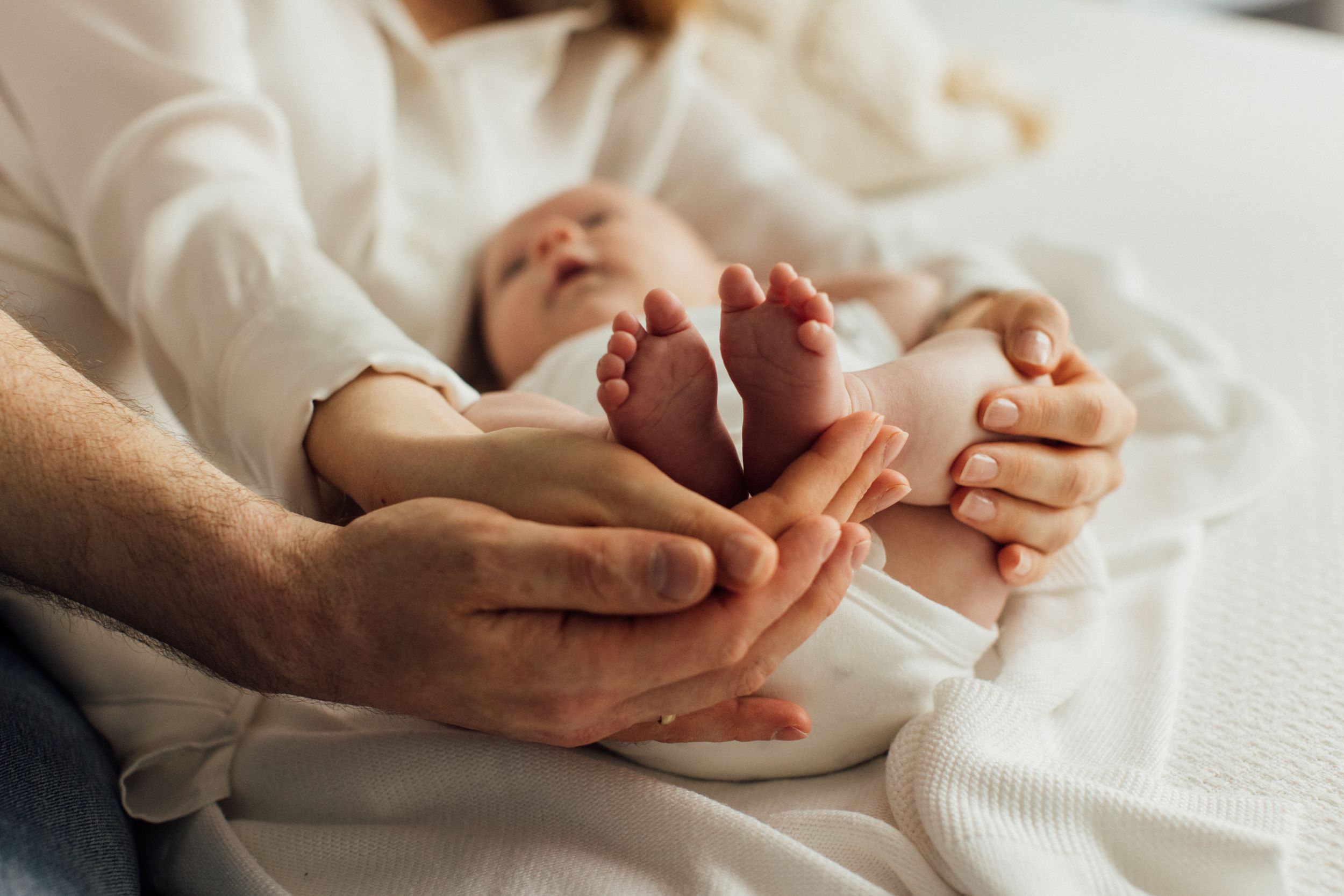Parents hands lovingly holding newborn baby feet on white blanket.