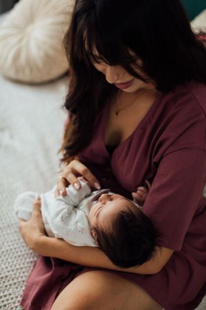 Mother in burgundy robe tenderly holding and gazing at her newborn baby.