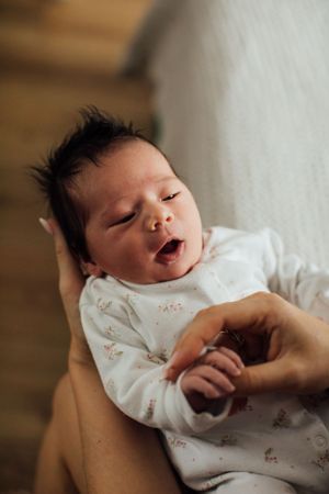Newborn baby yawning while being cradled in a parent's arms, wearing a white floral onesie.