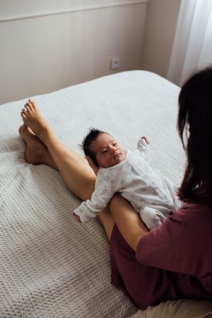 Newborn baby lying on bed resting on mothers legs looking upward.