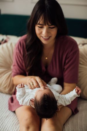 Smiling mother in burgundy dress looking down at her newborn baby resting on her lap.