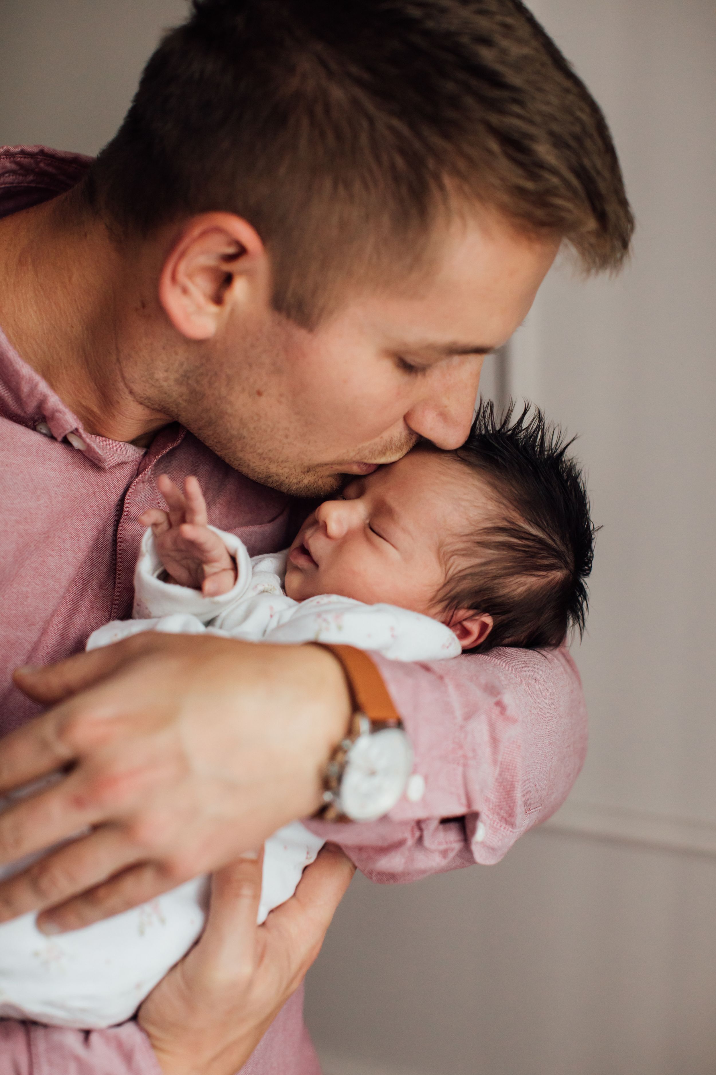 Father tenderly kissing his newborn baby on the forehead while holding the infant close.