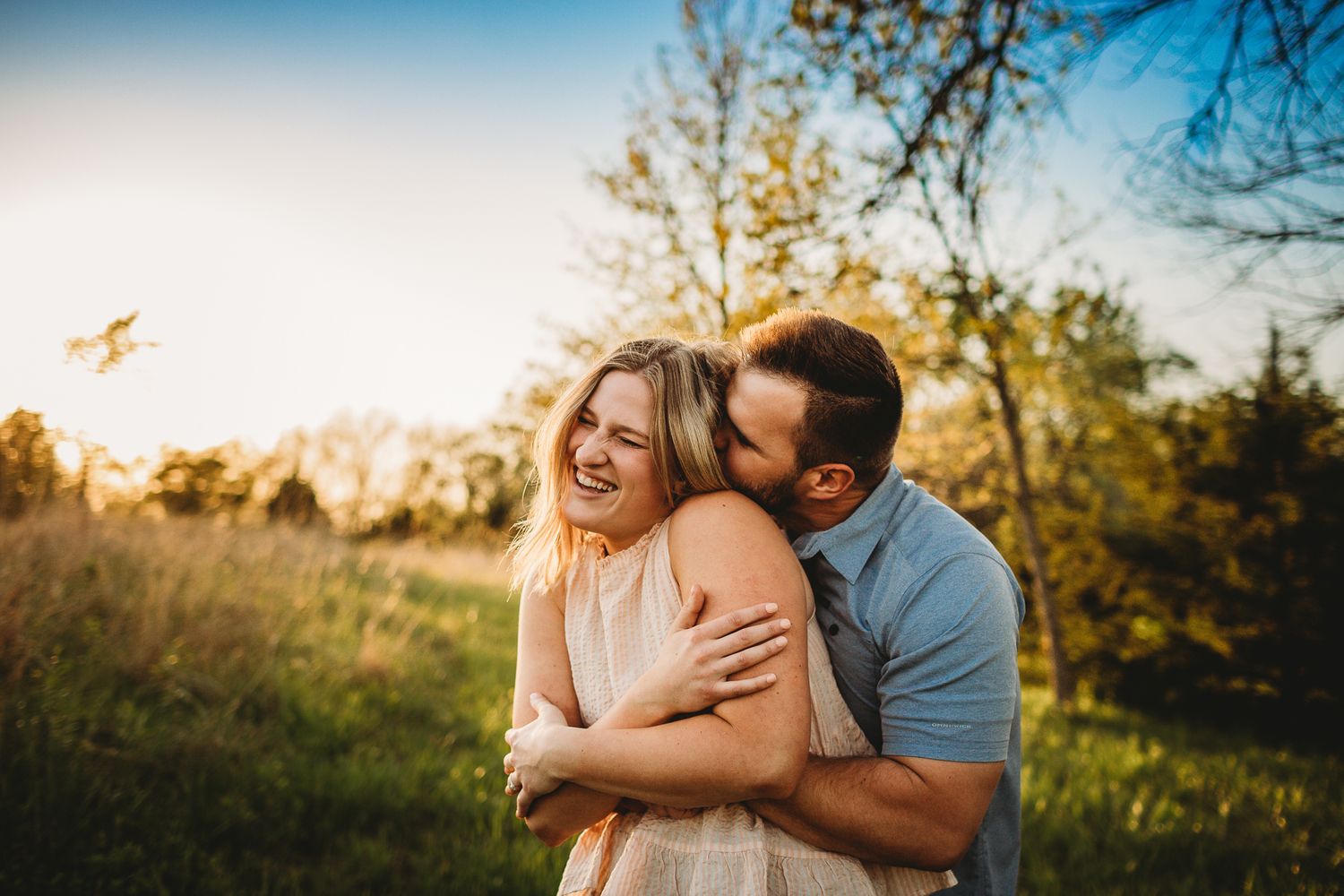Couple embracing and laughing together in a sunny golden field during an outdoor engagement photo session.