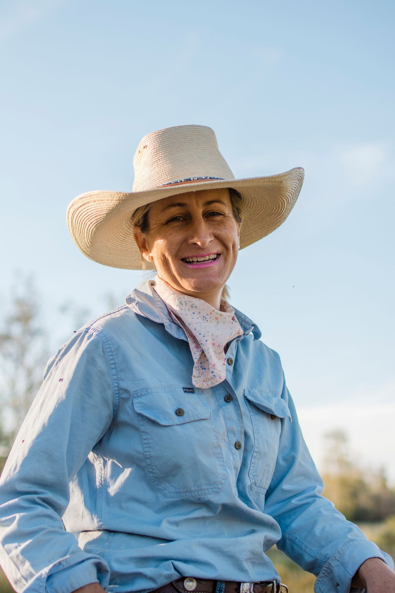 Jill Kelly in a blue workshirt with a lou webb hat,  on horseback with rural landscape