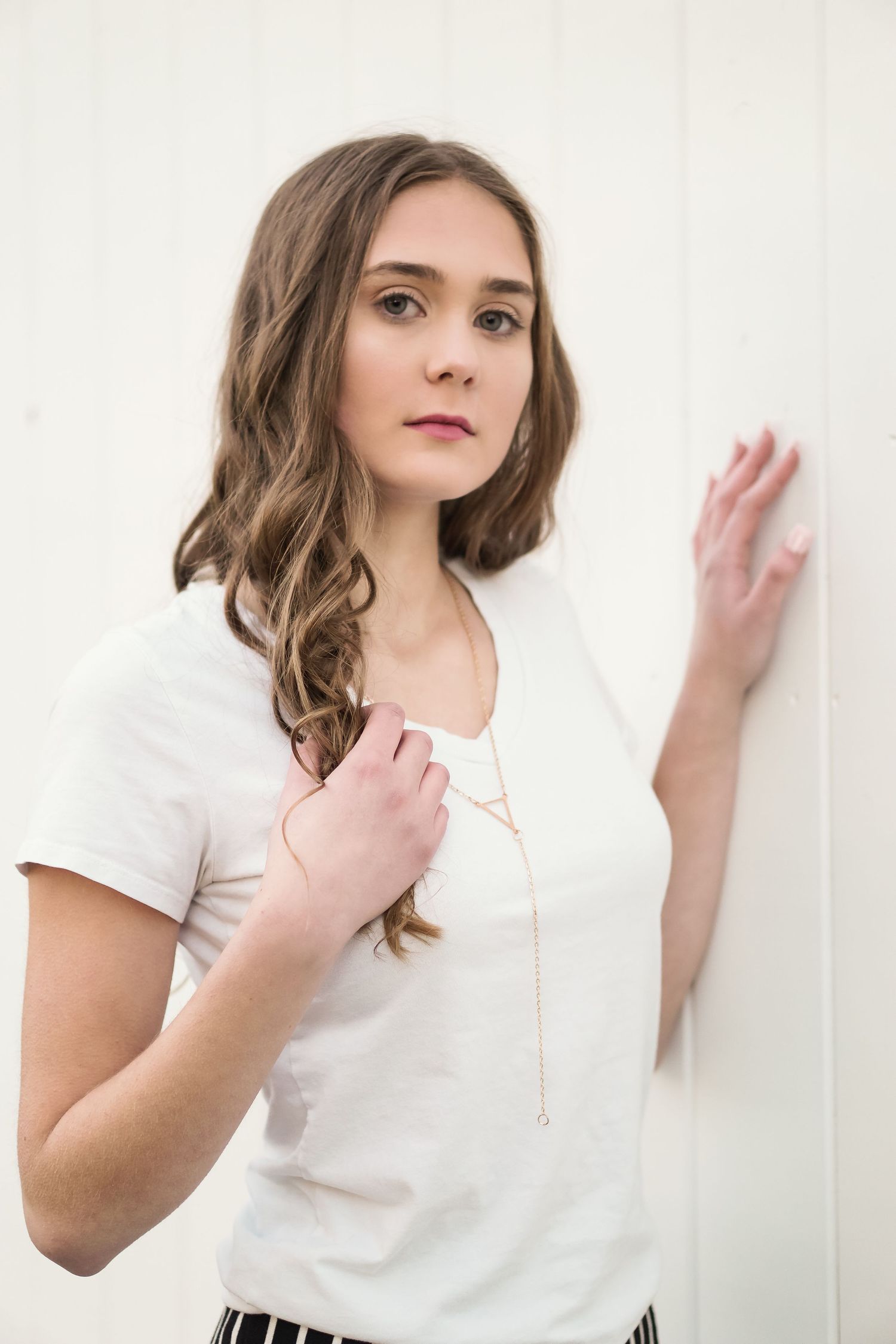 Woman in white top poses against white wall with soft natural lighting.