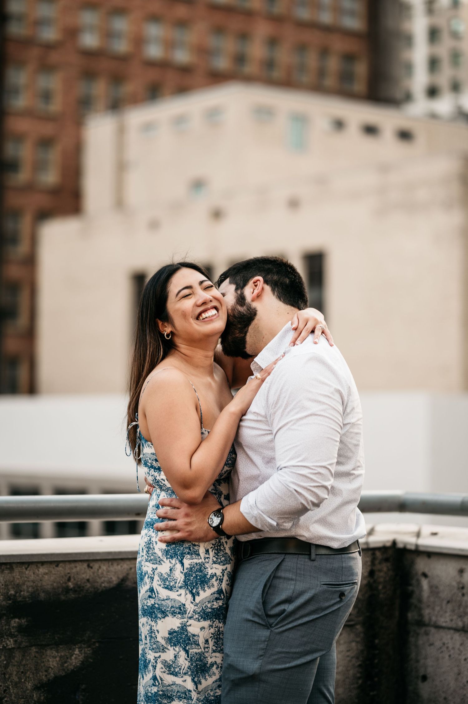 A couple laughs together on an urban rooftop during a romantic moment.