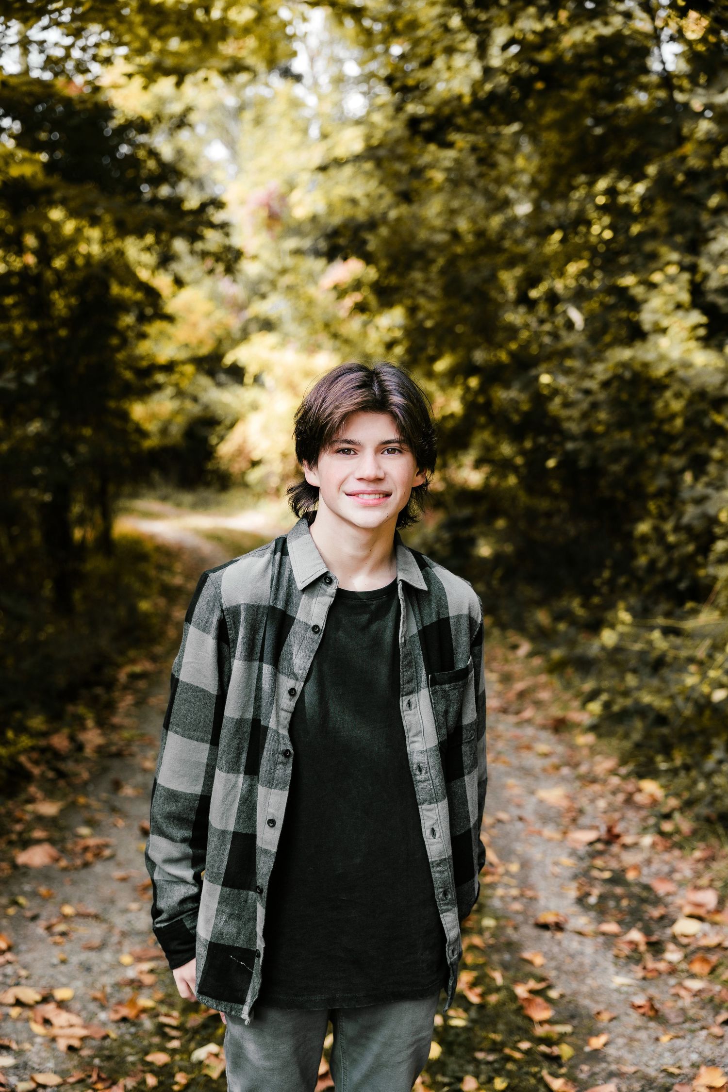 Autumn outdoor portrait on leaf-covered path wearing plaid flannel shirt.