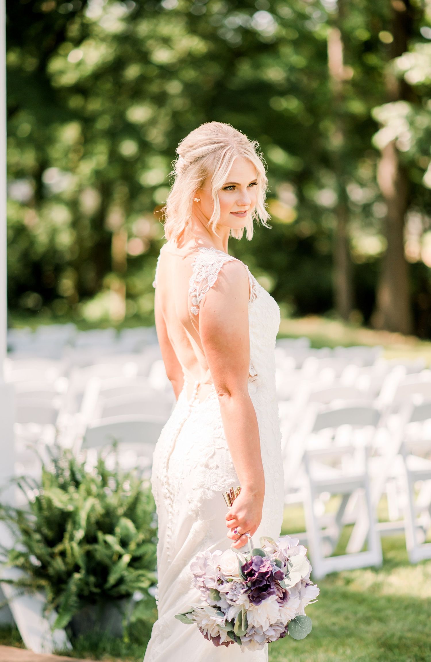 Bride in lace gown poses with purple bouquet at outdoor ceremony venue. Indianapolis, Indiana. Angela Hartwig Photography.