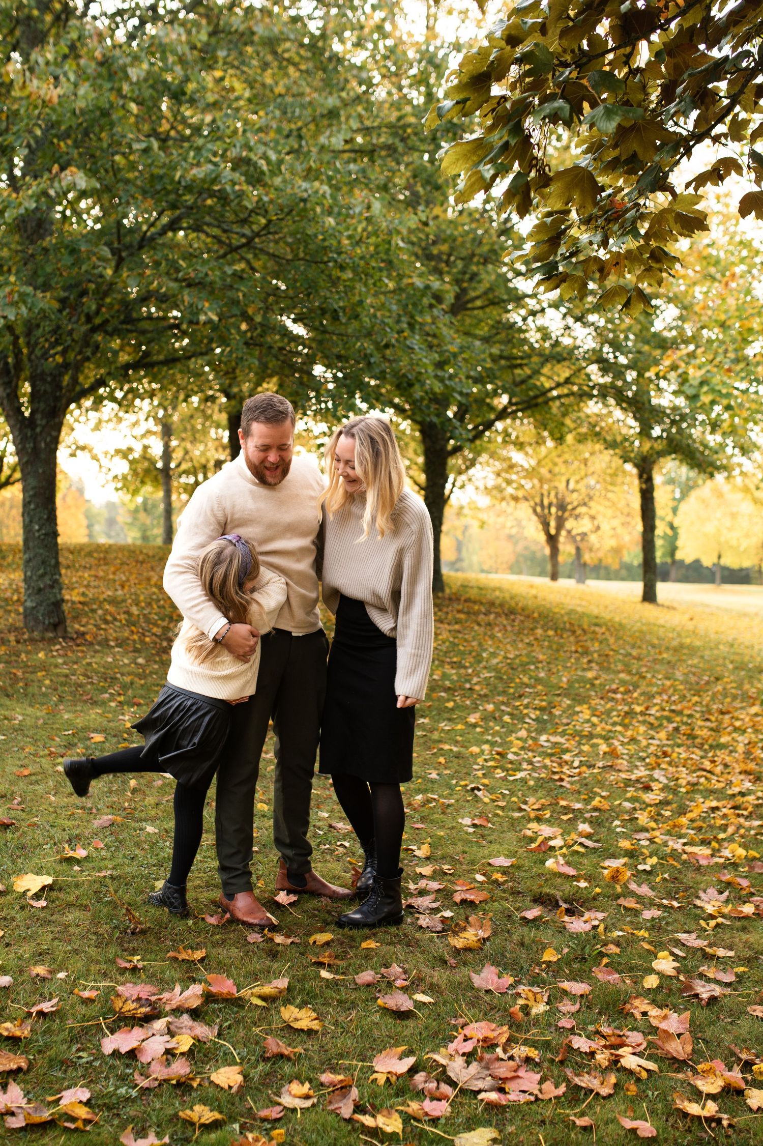 Family of three enjoying autumn weather in a park with fallen leaves.