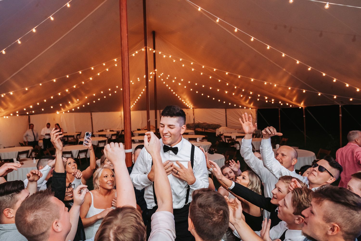 wedding tent dance floor photography of a grateful groom surrounded by cheering guests.