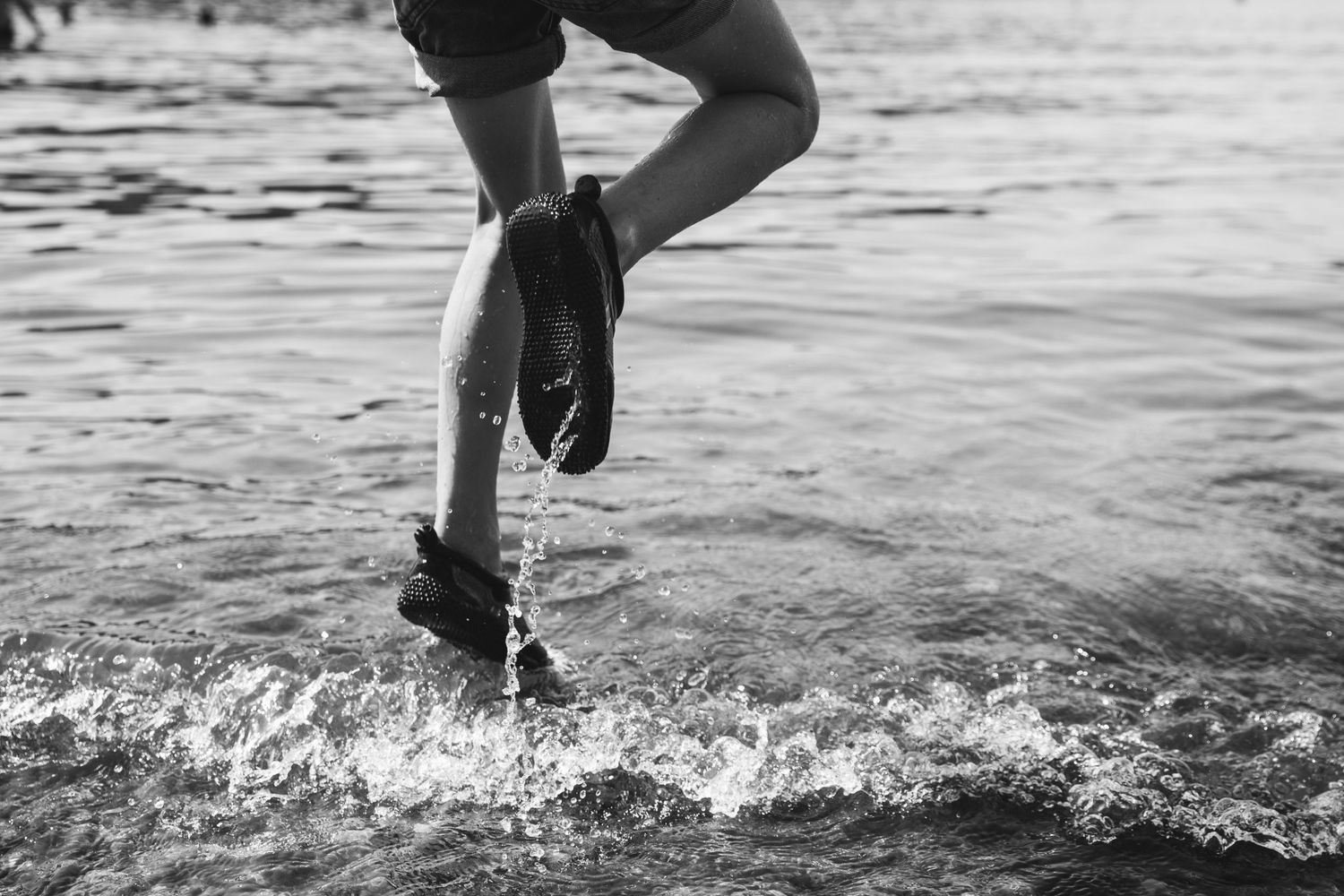 Black and white photo of legs splashing through shallow water.