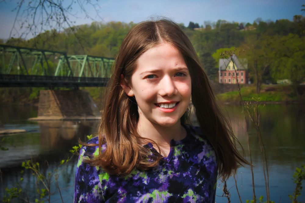 A person in a floral dress poses by a green bridge over water.